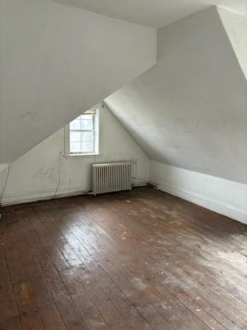 additional living space featuring dark wood-type flooring, radiator heating unit, and vaulted ceiling