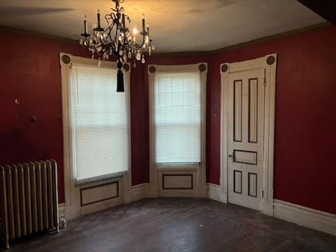 unfurnished dining area featuring a notable chandelier, crown molding, dark hardwood / wood-style floors, and radiator heating unit