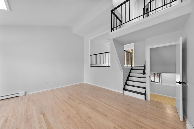 unfurnished living room with a towering ceiling, light hardwood / wood-style flooring, and a baseboard heating unit