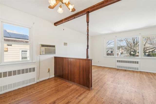 unfurnished room featuring radiator, a wall unit AC, light wood-type flooring, and beamed ceiling