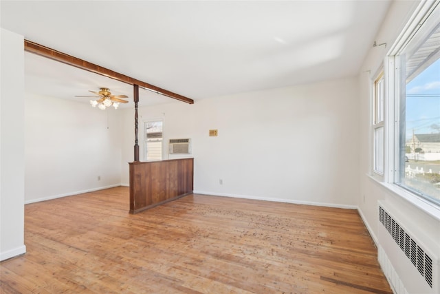 unfurnished living room featuring a healthy amount of sunlight, radiator heating unit, beam ceiling, and light hardwood / wood-style flooring