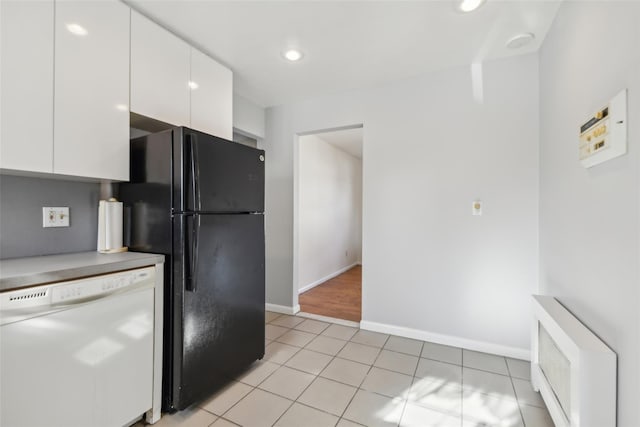 kitchen featuring radiator, dishwasher, white cabinets, light tile patterned floors, and black fridge