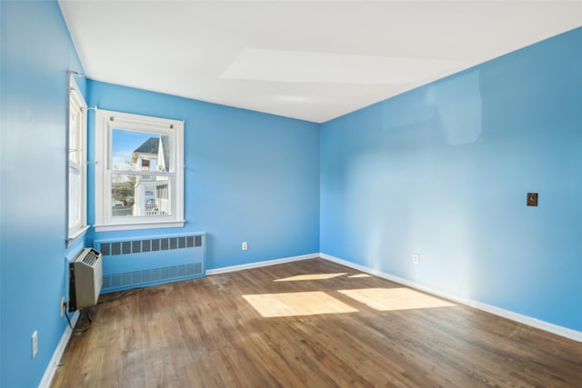 unfurnished room featuring radiator heating unit and hardwood / wood-style floors