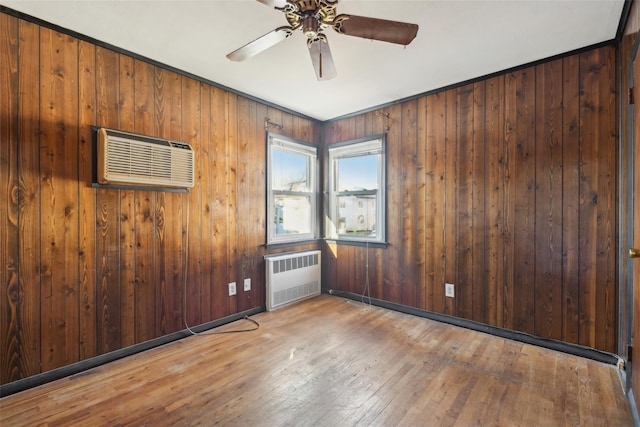 spare room featuring hardwood / wood-style flooring, ceiling fan, radiator heating unit, wooden walls, and a wall mounted air conditioner