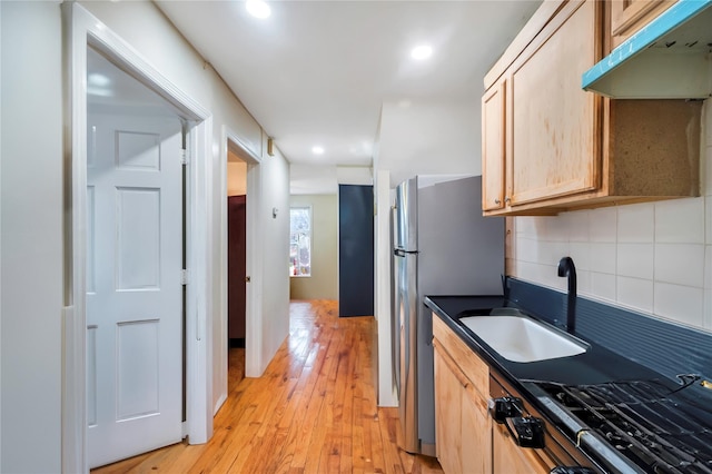 kitchen with light brown cabinets, tasteful backsplash, light wood-type flooring, stovetop, and sink