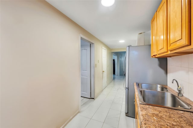 kitchen featuring light stone countertops, stainless steel refrigerator, and sink