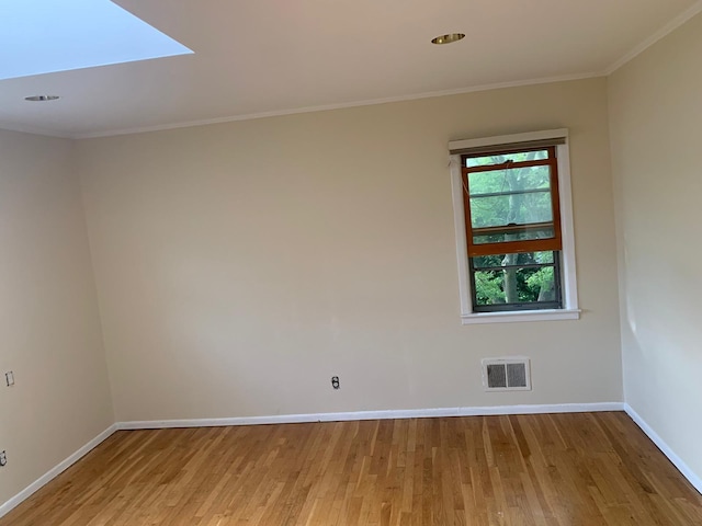 unfurnished room with a skylight, ornamental molding, and light hardwood / wood-style floors