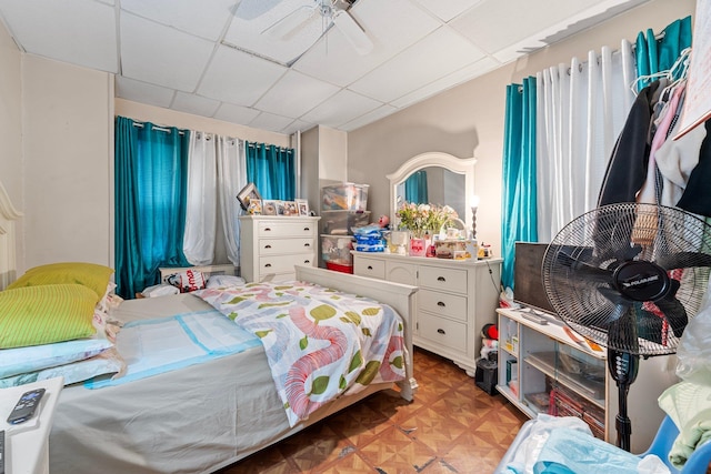 bedroom featuring ceiling fan, a drop ceiling, and light parquet floors