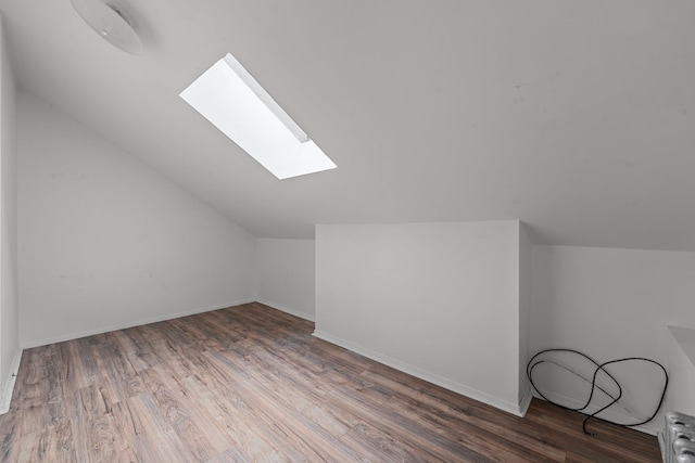 additional living space with radiator, vaulted ceiling with skylight, and dark wood-type flooring