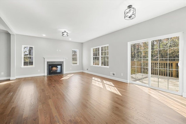 unfurnished living room with a tile fireplace, a wealth of natural light, a notable chandelier, and hardwood / wood-style flooring