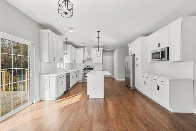 kitchen featuring appliances with stainless steel finishes, wall chimney exhaust hood, pendant lighting, a center island, and white cabinetry