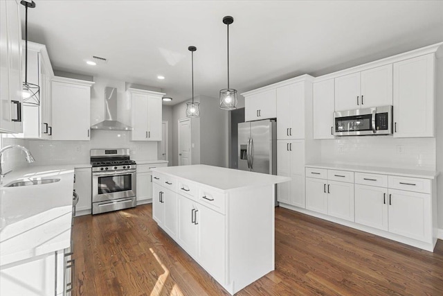 kitchen featuring appliances with stainless steel finishes, wall chimney exhaust hood, sink, white cabinets, and a center island