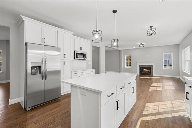 kitchen with dark wood-type flooring, white cabinets, hanging light fixtures, a kitchen island, and stainless steel appliances