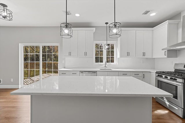 kitchen featuring white cabinetry, wall chimney exhaust hood, hanging light fixtures, stainless steel appliances, and a kitchen island