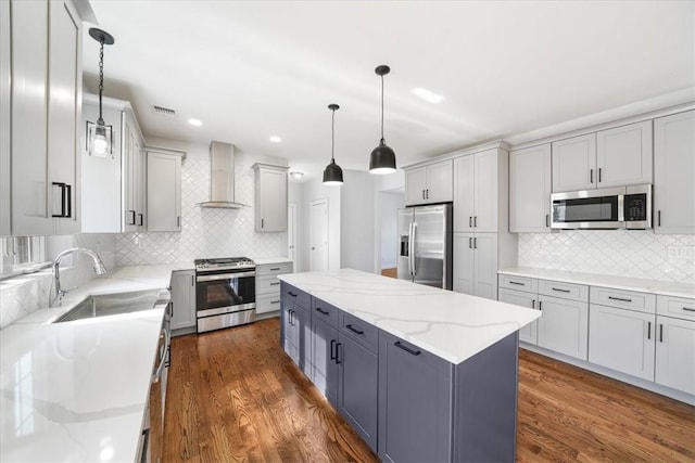 kitchen with pendant lighting, a center island, sink, wall chimney exhaust hood, and appliances with stainless steel finishes