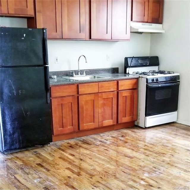 kitchen with white range with gas cooktop, black refrigerator, light hardwood / wood-style floors, and sink