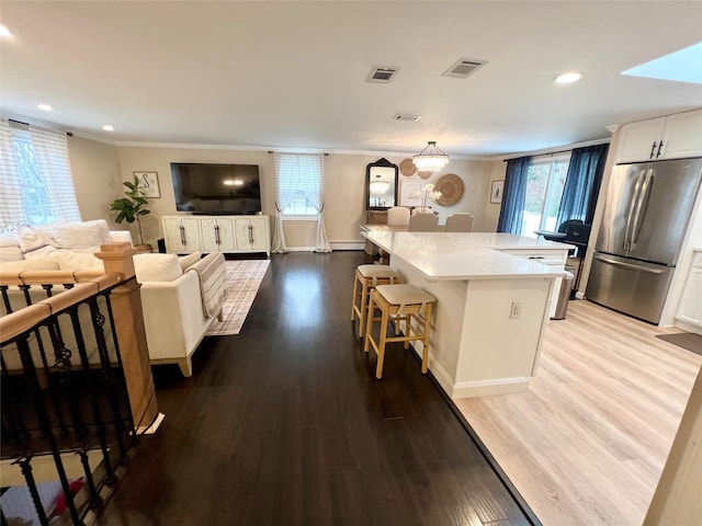 kitchen featuring stainless steel refrigerator, a kitchen breakfast bar, white cabinets, a kitchen island, and light wood-type flooring