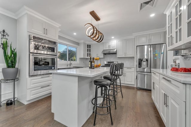 kitchen featuring pendant lighting, a kitchen island, crown molding, white cabinetry, and stainless steel appliances