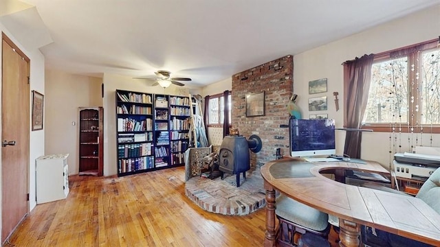 office space featuring a wood stove, ceiling fan, plenty of natural light, and light hardwood / wood-style flooring