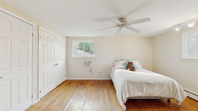 bedroom with two closets, heating unit, ceiling fan, a baseboard heating unit, and light hardwood / wood-style floors