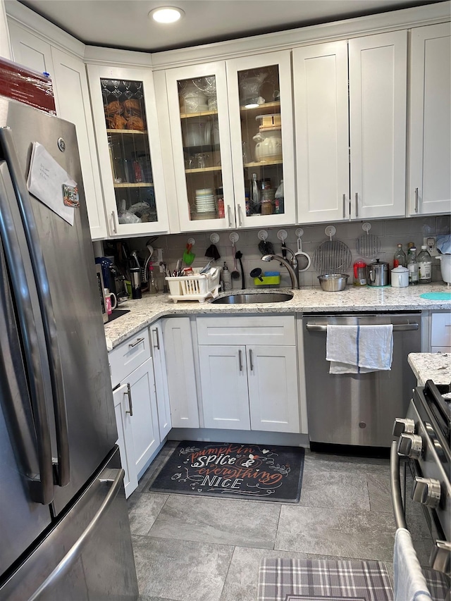 kitchen with sink, backsplash, white cabinets, light stone counters, and stainless steel appliances