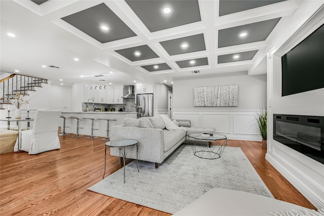 living room with beamed ceiling, ornamental molding, light hardwood / wood-style floors, and coffered ceiling