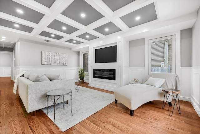 living room featuring beam ceiling, light wood-type flooring, a fireplace, and coffered ceiling