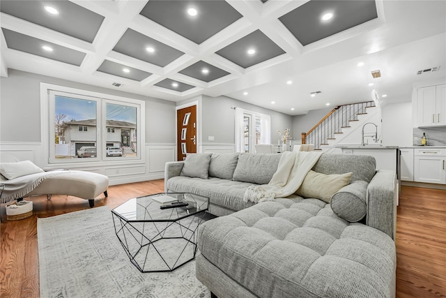 living room featuring beam ceiling, light hardwood / wood-style flooring, coffered ceiling, and sink