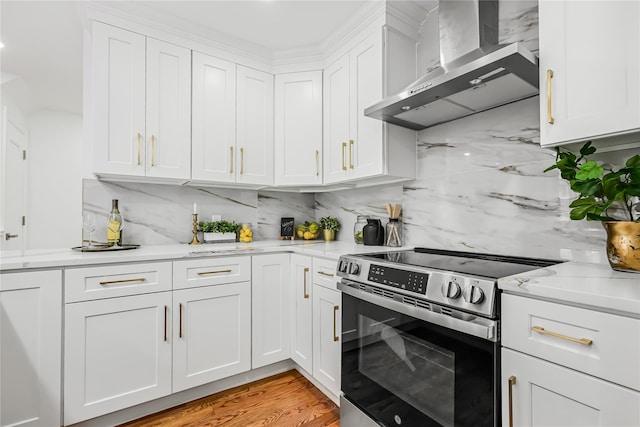 kitchen with stainless steel electric range oven, white cabinets, light hardwood / wood-style floors, and wall chimney range hood