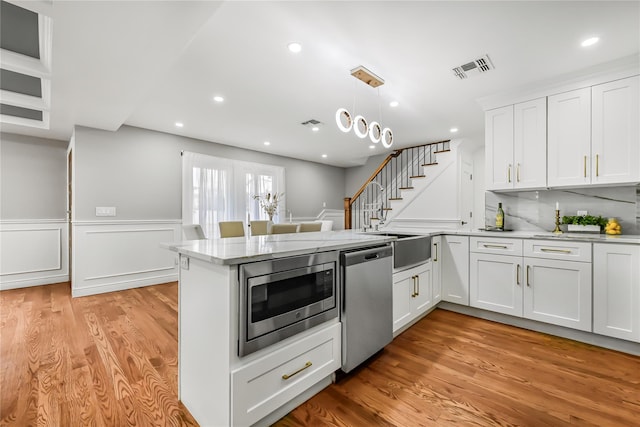 kitchen featuring kitchen peninsula, pendant lighting, white cabinets, and stainless steel appliances