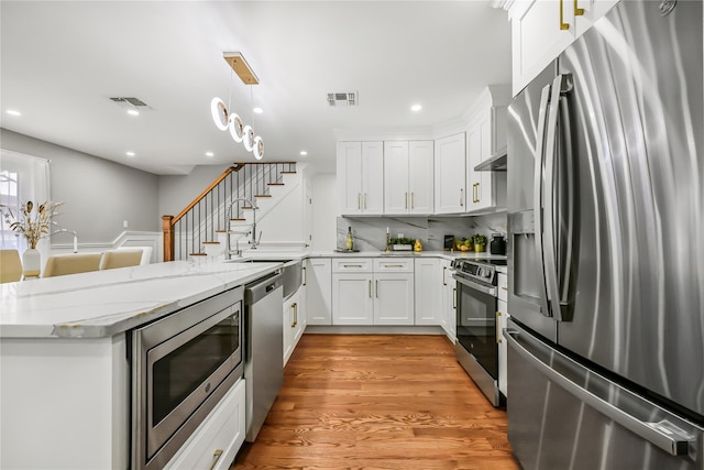 kitchen featuring kitchen peninsula, stainless steel appliances, pendant lighting, light hardwood / wood-style flooring, and white cabinetry