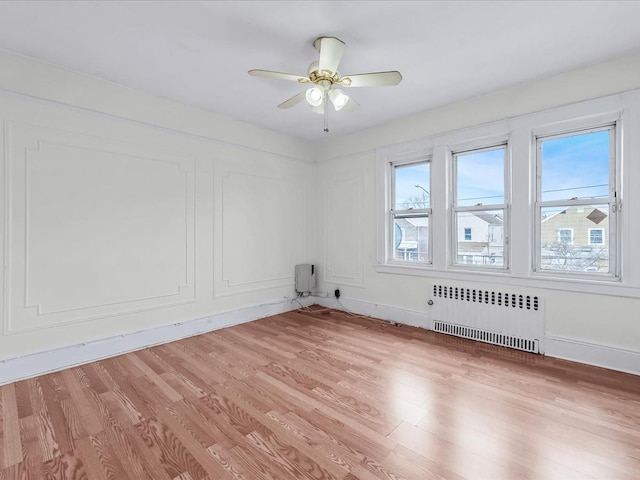 empty room with radiator heating unit, ceiling fan, and light hardwood / wood-style floors