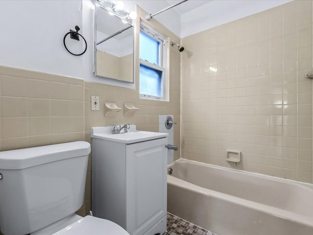 full bathroom with tile walls, tiled shower / bath, vanity, and toilet