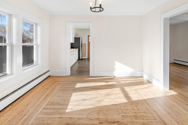 unfurnished dining area featuring a baseboard radiator, a chandelier, and light wood-type flooring