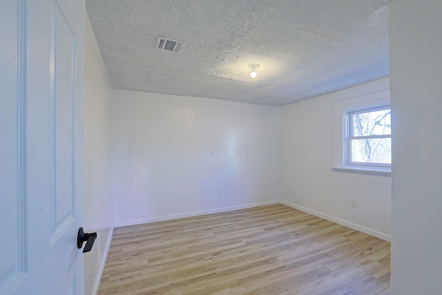 empty room with a textured ceiling and light hardwood / wood-style flooring