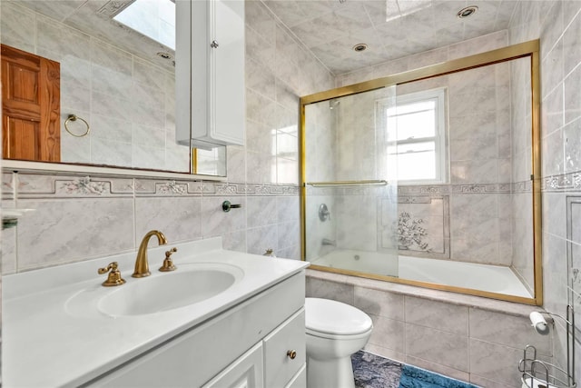 full bathroom featuring vanity, toilet, combined bath / shower with glass door, and tile walls