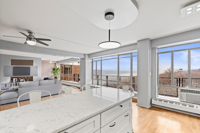 kitchen featuring white cabinets, open floor plan, decorative light fixtures, light stone countertops, and light wood-style floors