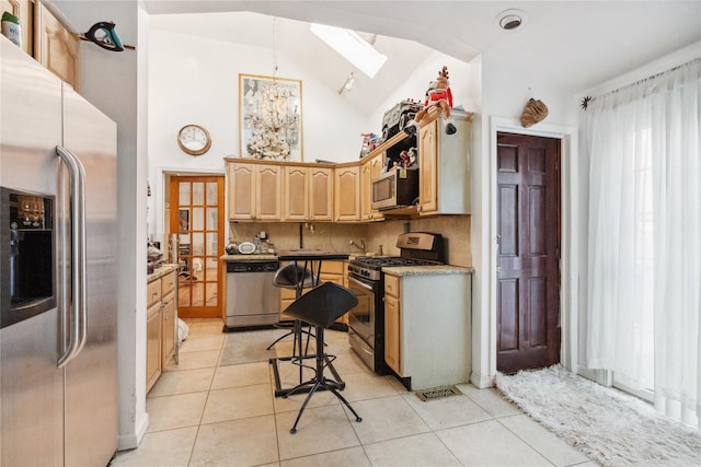 kitchen with light brown cabinets, lofted ceiling with skylight, backsplash, light tile patterned floors, and stainless steel appliances