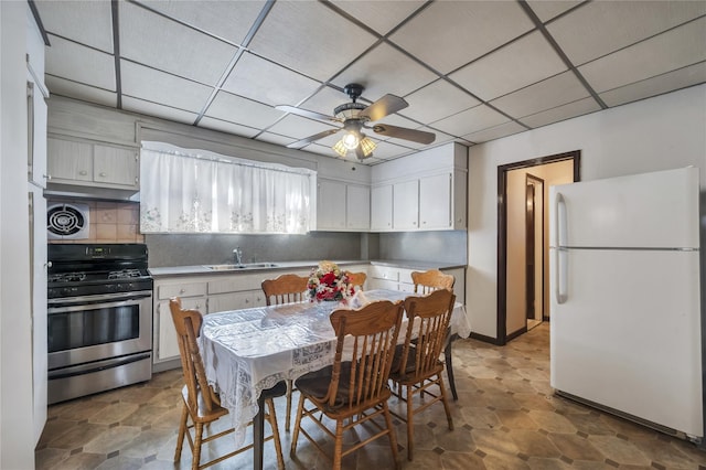 kitchen with tasteful backsplash, a drop ceiling, stainless steel gas range, white fridge, and white cabinetry