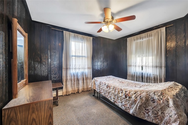 carpeted bedroom featuring baseboard heating, ceiling fan, and wood walls