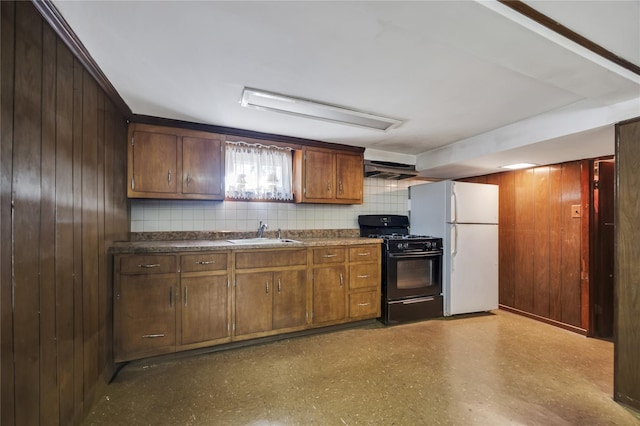 kitchen featuring sink, black range with gas stovetop, range hood, white refrigerator, and wood walls