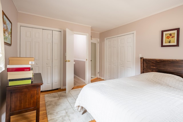 bedroom featuring ornamental molding, two closets, and light hardwood / wood-style floors