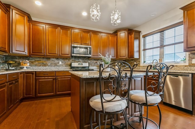 kitchen with light stone countertops, hanging light fixtures, a center island, stainless steel appliances, and dark hardwood / wood-style flooring