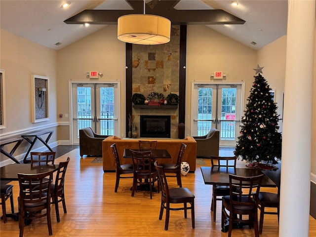 dining room featuring high vaulted ceiling, french doors, light wood-type flooring, and a fireplace