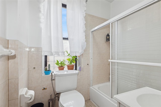 bathroom featuring shower / bath combination with glass door, toilet, and tile walls