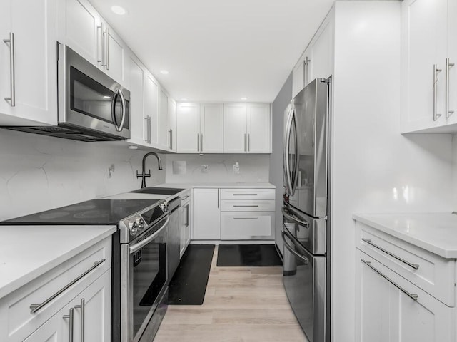 kitchen featuring sink, light hardwood / wood-style flooring, tasteful backsplash, white cabinetry, and stainless steel appliances