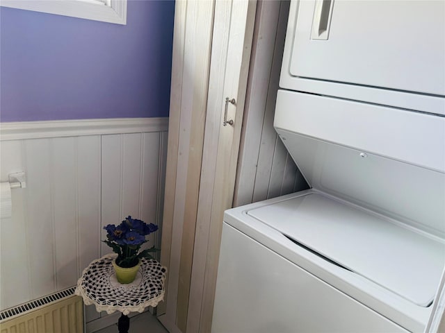 clothes washing area featuring radiator heating unit and stacked washing maching and dryer