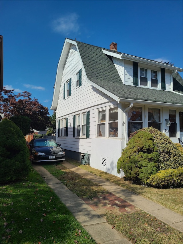 view of front facade with a shingled roof, a chimney, and a gambrel roof