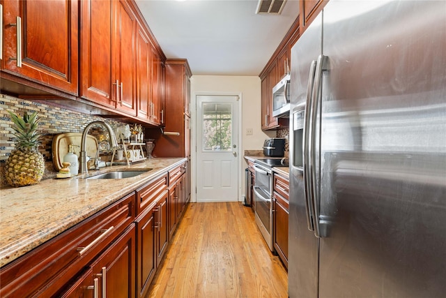 kitchen with backsplash, light stone counters, stainless steel appliances, sink, and light hardwood / wood-style flooring