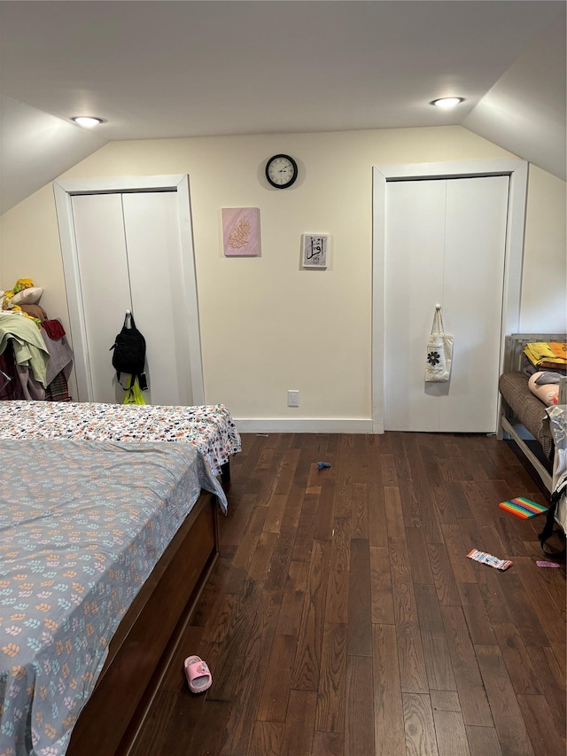 bedroom featuring two closets, dark wood-type flooring, and vaulted ceiling